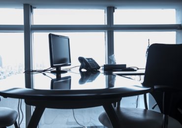 black and white photo of an empty office desk and chair with a monitor and telephone on the table (company_retrenchment_asia_law_network)