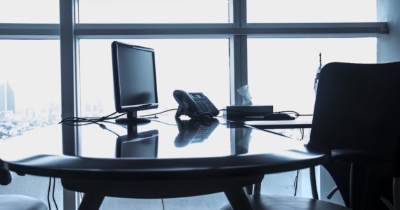 black and white photo of an empty office desk and chair with a monitor and telephone on the table (company_retrenchment_asia_law_network)