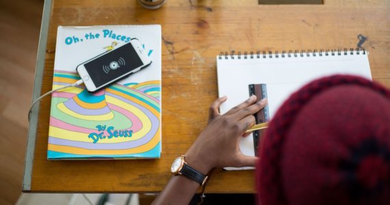 a man drawing on paper with a ruler on it. left of table has an iphone on a book by Dr Seuss (copyright_law_singapore_asia_law_network)