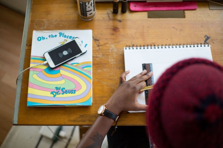 a man drawing on paper with a ruler on it. left of table has an iphone on a book by Dr Seuss (copyright_law_singapore_asia_law_network)