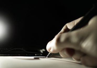 black and white photo of a hand holding a pen and writing on a paper (writing a will)
