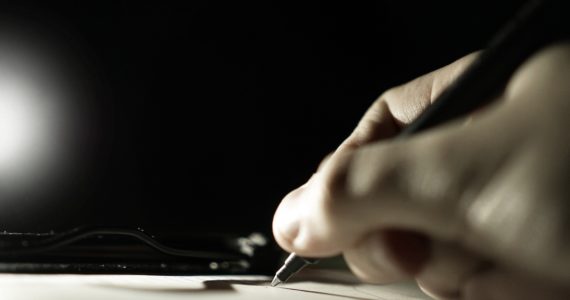 black and white photo of a hand holding a pen and writing on a paper (writing a will)