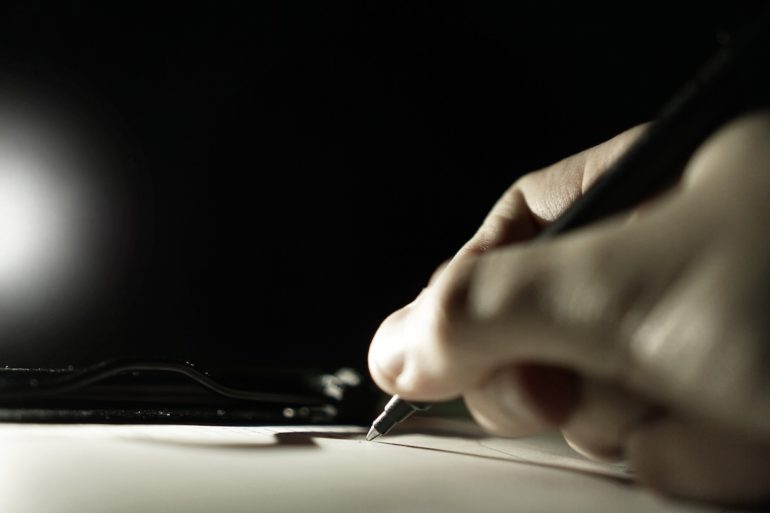 black and white photo of a hand holding a pen and writing on a paper (writing a will)