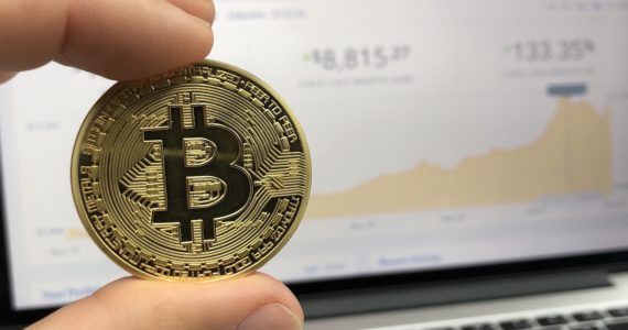 bitcoin against a laptop of stocks charts (Cryptocurrency)