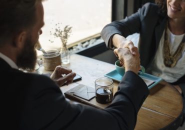 business man and woman shaking hands over a table with 2 cups of coffee (What constitutes acceptance of a contract)