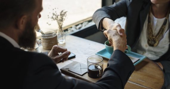 business man and woman shaking hands over a table with 2 cups of coffee (What constitutes acceptance of a contract)