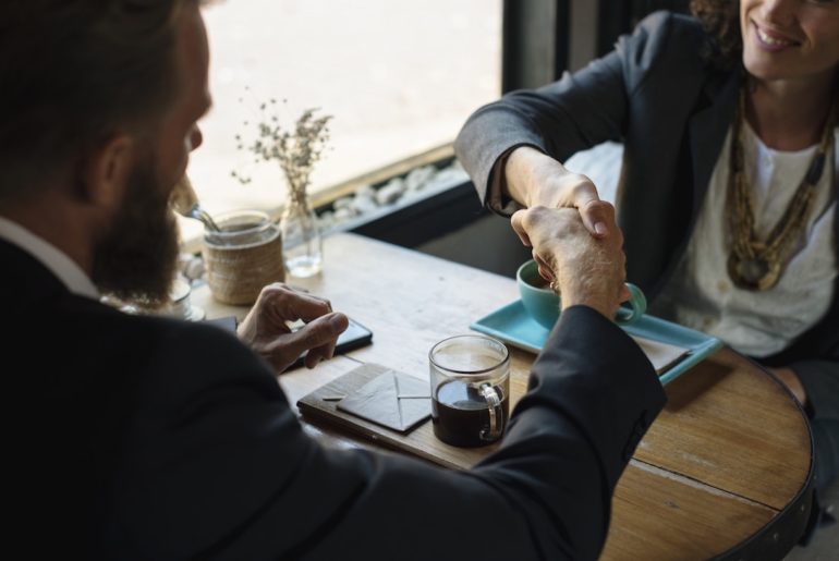 business man and woman shaking hands over a table with 2 cups of coffee (What constitutes acceptance of a contract)