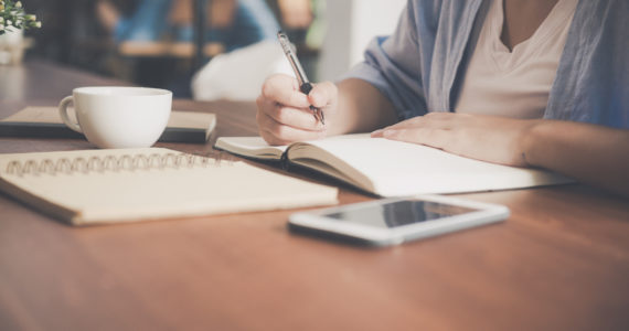 Young business woman in white dress sitting at table in cafe and writing in notebook. Asian woman talking smartphone and cup of coffee. Freelancer working in coffee shop. Vintage effect style pictures (Intestacy - Dying Without a Will_Asia_Law_Network)