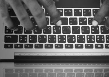 black and white photo of a macbook keyboard with a hand typing on it (white_collar_crime_asia_law_network_criminal_breach_of_trust)