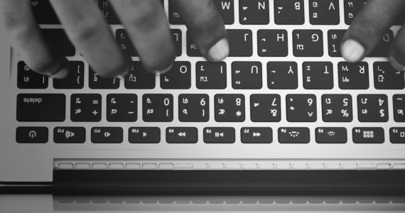 black and white photo of a macbook keyboard with a hand typing on it (white_collar_crime_asia_law_network_criminal_breach_of_trust)